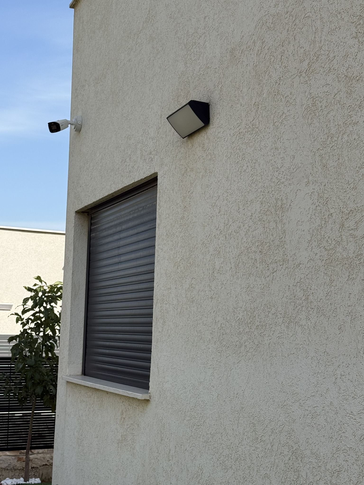 מצלמת אבטחה ותאורת חוץ מותקנות על קיר בית פרטי